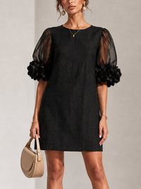 Vestido corto negro de organza con mangas abullonadas y puños florales llamativos.